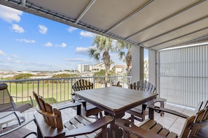 A covered patio with a wooden table and chairs, overlooking a golf course and buildings. - Magnolia House 112 2 Bedroom Condo by RedAwning (Destin)