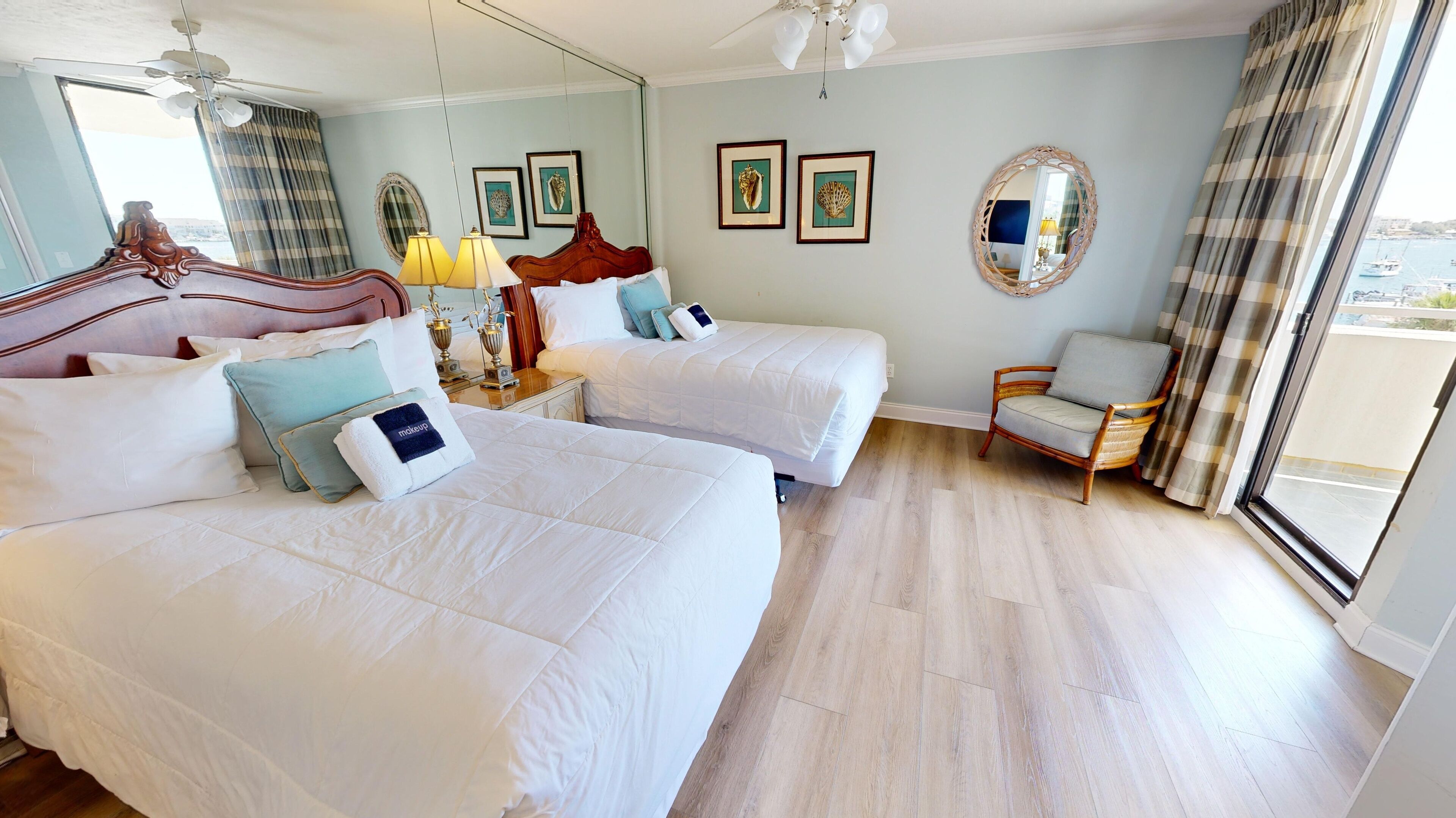 A hotel room with two beds, a chair, and a balcony with a view.