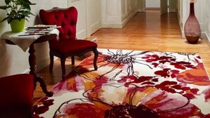 A hallway with a red chair, a table with a plant, and a floral rug. - Chambres d'hotes du Parc (Podensac)