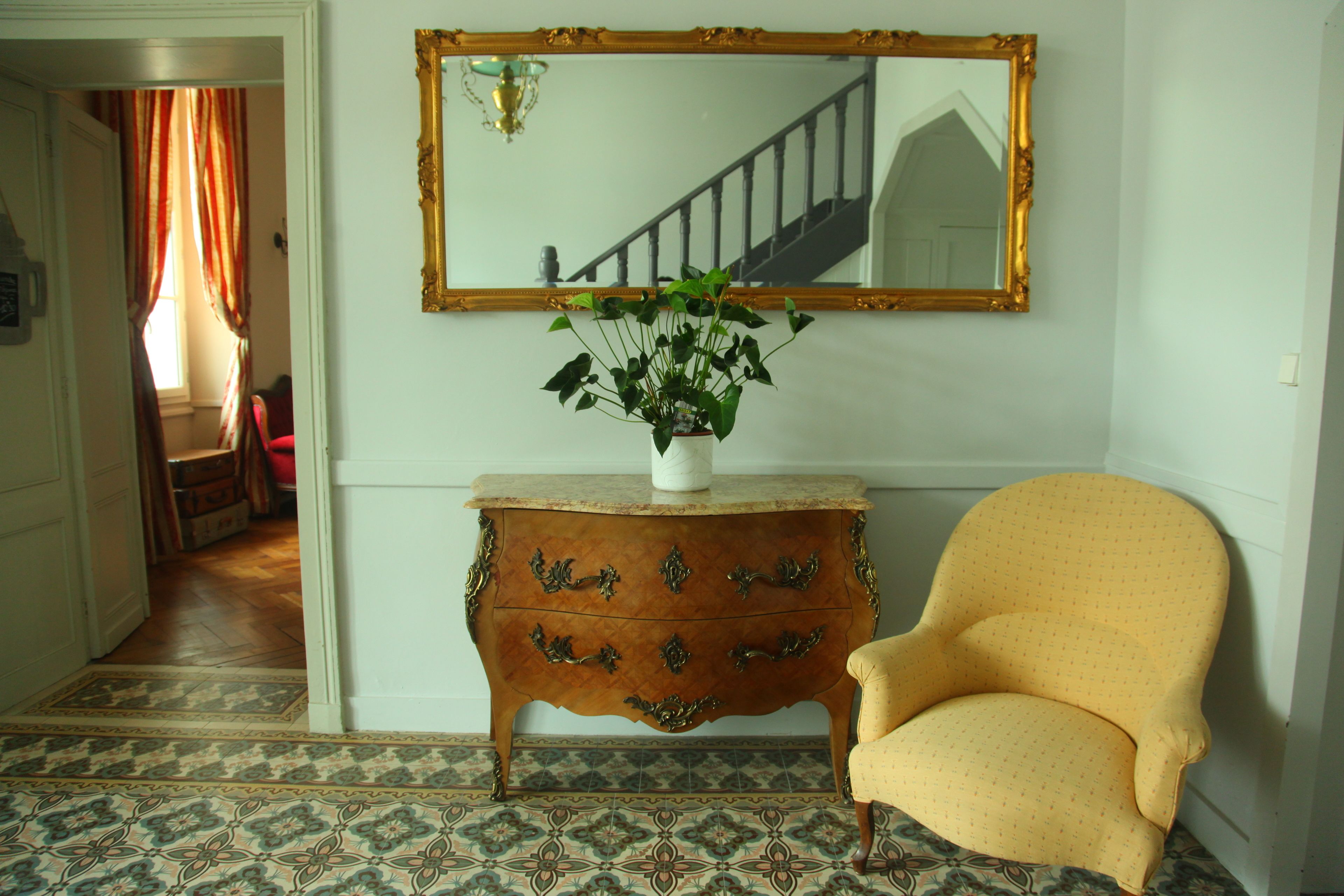 Una habitación con un aparador de madera, un sillón amarillo, un espejo grande y una planta en maceta.