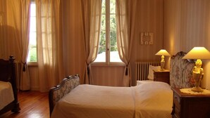 A bedroom with a large bed, two bedside tables, a nightstand, and a window with curtains. - Chambres d'hotes du Parc (Podensac)