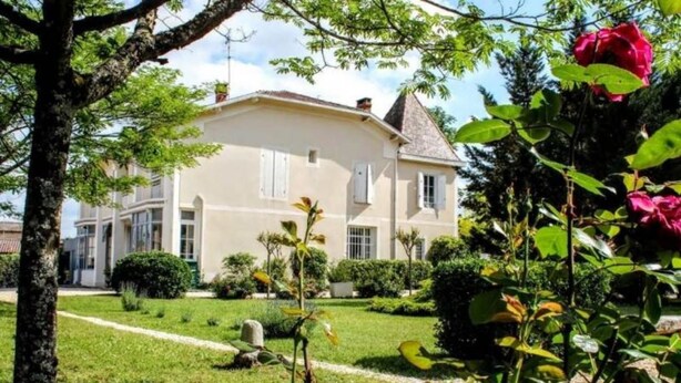 A two-story building with a symmetrical facade, a central entrance, and a well-maintained garden with various plants and a prominent red flower. - Chambres d'hotes du Parc (Podensac)