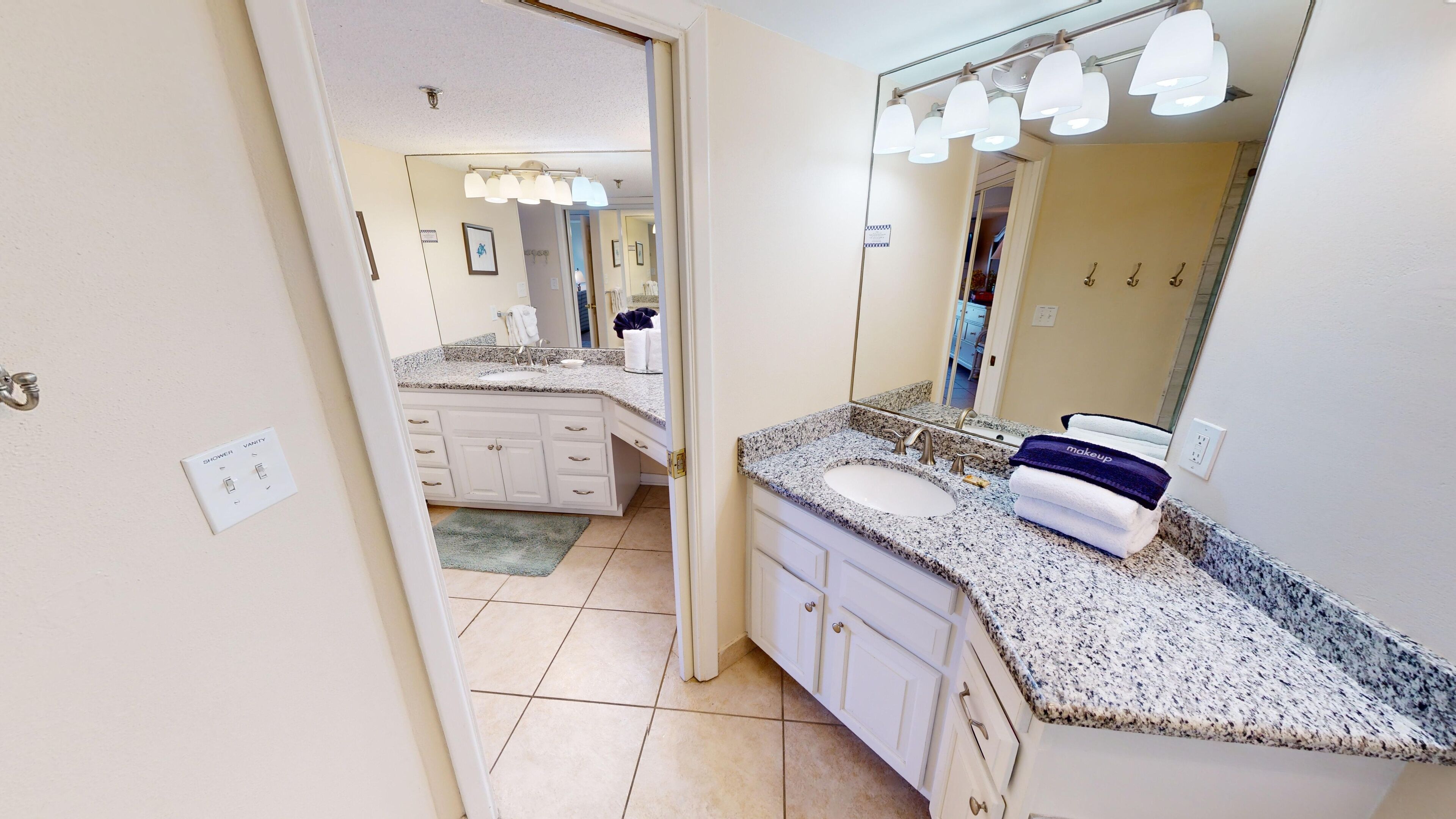 Une salle de bain moderne avec des comptoirs en granit, un meuble-lavabo à deux vasques et un grand miroir avec un éclairage intégré au-dessus.