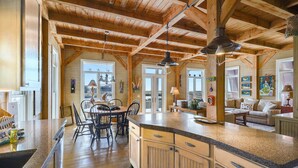Une cuisine spacieuse avec des poutres apparentes, un grand îlot central doté d’un plan de travail en granit, et un coin repas avec des chaises et une table.