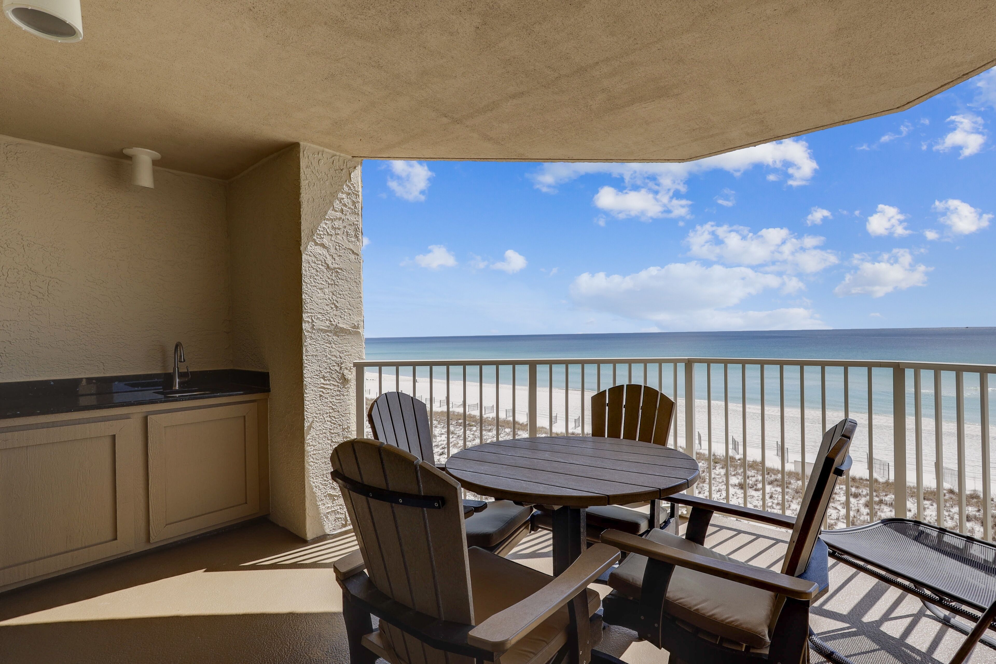 Un balcon donnant sur la plage, une table ronde et des chaises en bois.
