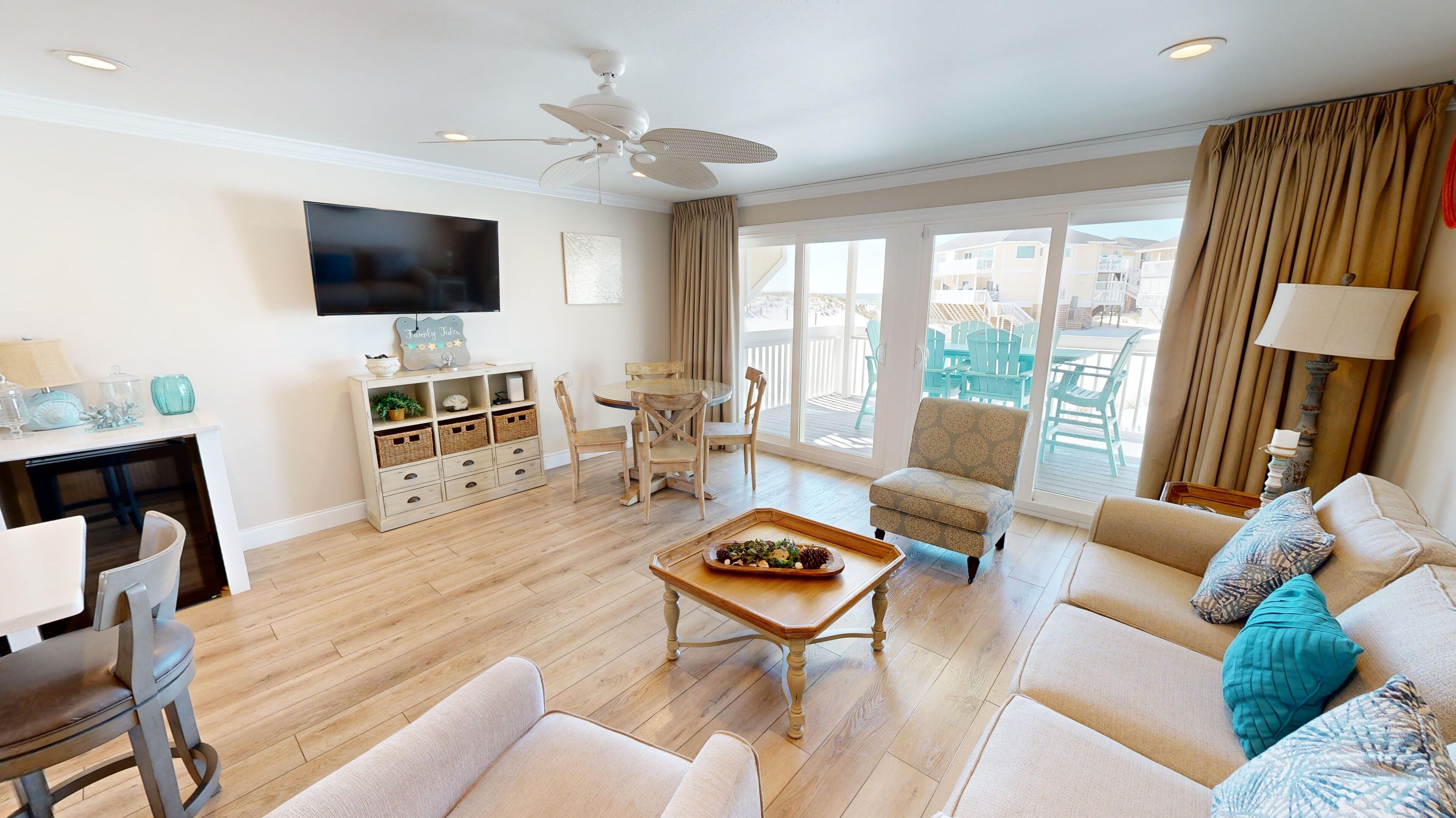Ein geräumiges Wohnzimmer mit Flachbildfernseher, Deckenventilator, Essbereich mit Tisch und Stühlen sowie Sofa mit Zierkissen.