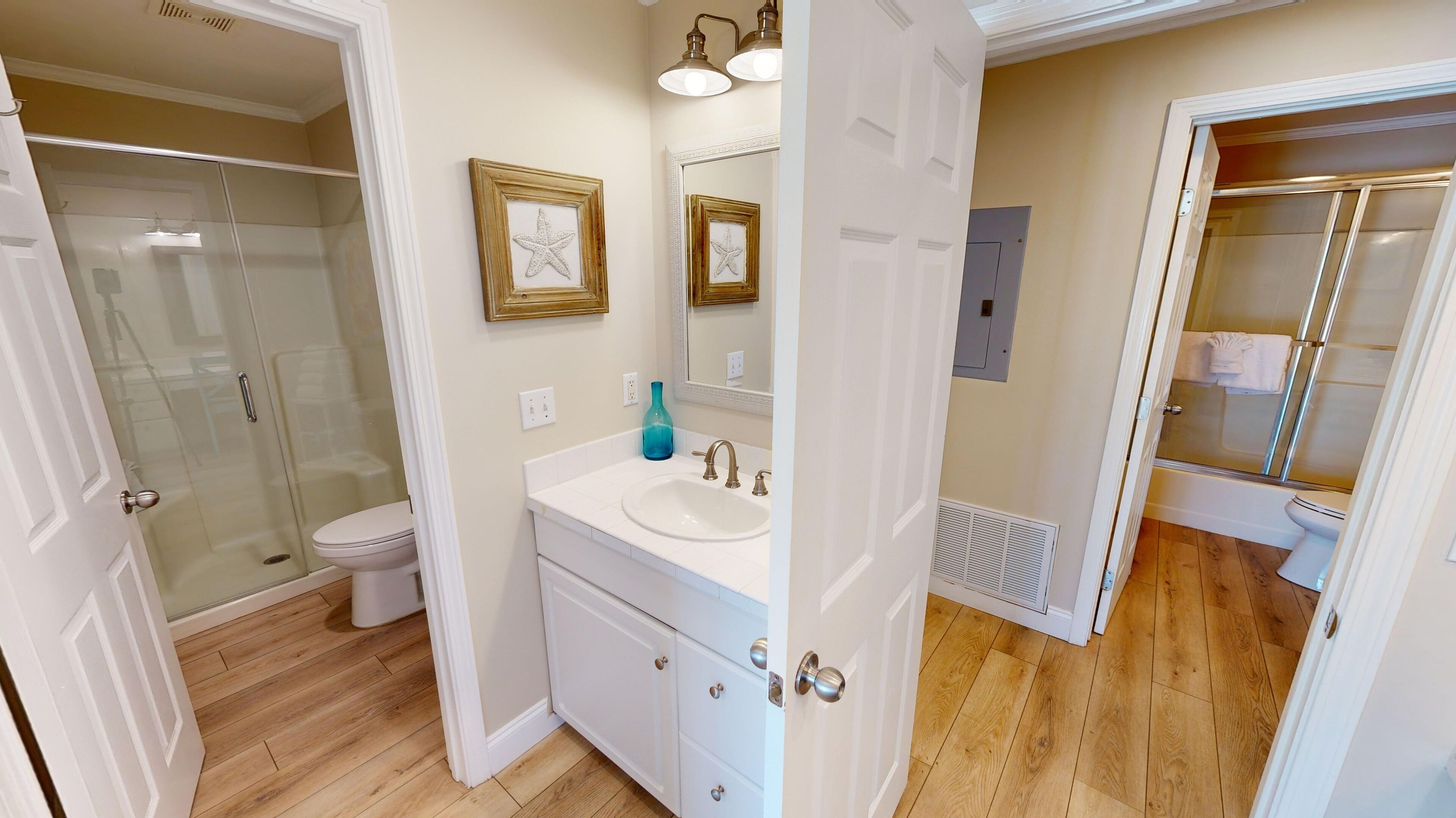A bathroom with a glass shower enclosure, a white sink with a gold faucet, and a mirror with a starfish decoration.