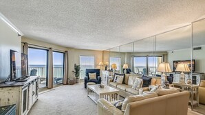 A spacious living room with a large sofa, a coffee table, and a TV. There is a balcony with a view of the ocean. - Inlet Reef 602 2 Bedroom Condo by RedAwning (Destin)