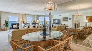 A spacious living room with a round glass table, wicker chairs, and a chandelier. - Inlet Reef 602 2 Bedroom Condo by RedAwning (Destin)