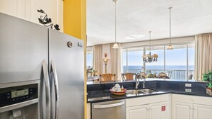 A modern kitchen with a stainless steel refrigerator, a built-in water dispenser, and a large window offering a view of the ocean. - Oceania 907 3 Bedroom Condo by RedAwning (Destin)