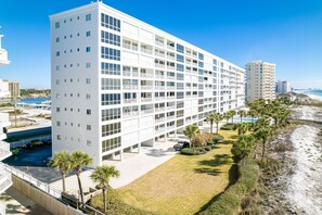 Ein mehrstöckiges Hotel mit weißer Fassade, Balkonen und einem Poolbereich mit Palmen.
