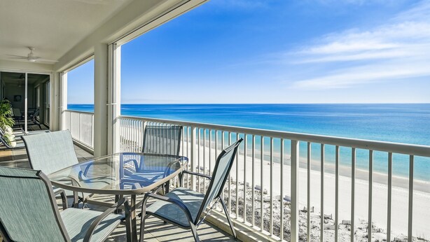 A balcony with a glass table and chairs, overlooking a beach with clear blue water and a sandy shore. - Oceania 907 3 Bedroom Condo by RedAwning (Destin)