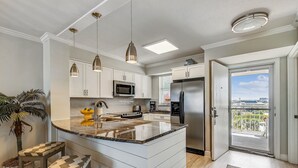 A modern kitchen with white cabinetry, a central island, pendant lighting, and a view through a glass door to the outdoors.