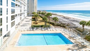 Een hotel met een zwembad, uitzicht op het strand en palmbomen.