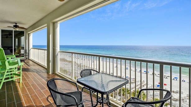 Een balkon met een tafel en stoelen, met uitzicht op een strand met parasols en mensen.