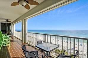 Een balkon met een tafel en stoelen, met uitzicht op een strand met parasols en mensen.