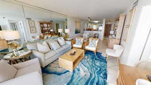 A spacious living room with a large grey sofa, two armchairs, a coffee table, and a dining area with a table and chairs. - Destin On The Gulf 505 2 Bedroom Condo by RedAwning (Destin)