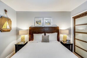 A neatly arranged hotel room with a wooden headboard, two bedside tables with lamps, a bed with white linens, and two framed pictures above the headboard. - Holiday Surf & Racquet 402 2 Bedroom Condo by RedAwning (Destin)