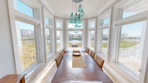 A long dining table with woven benches, large windows, and hanging light fixtures.