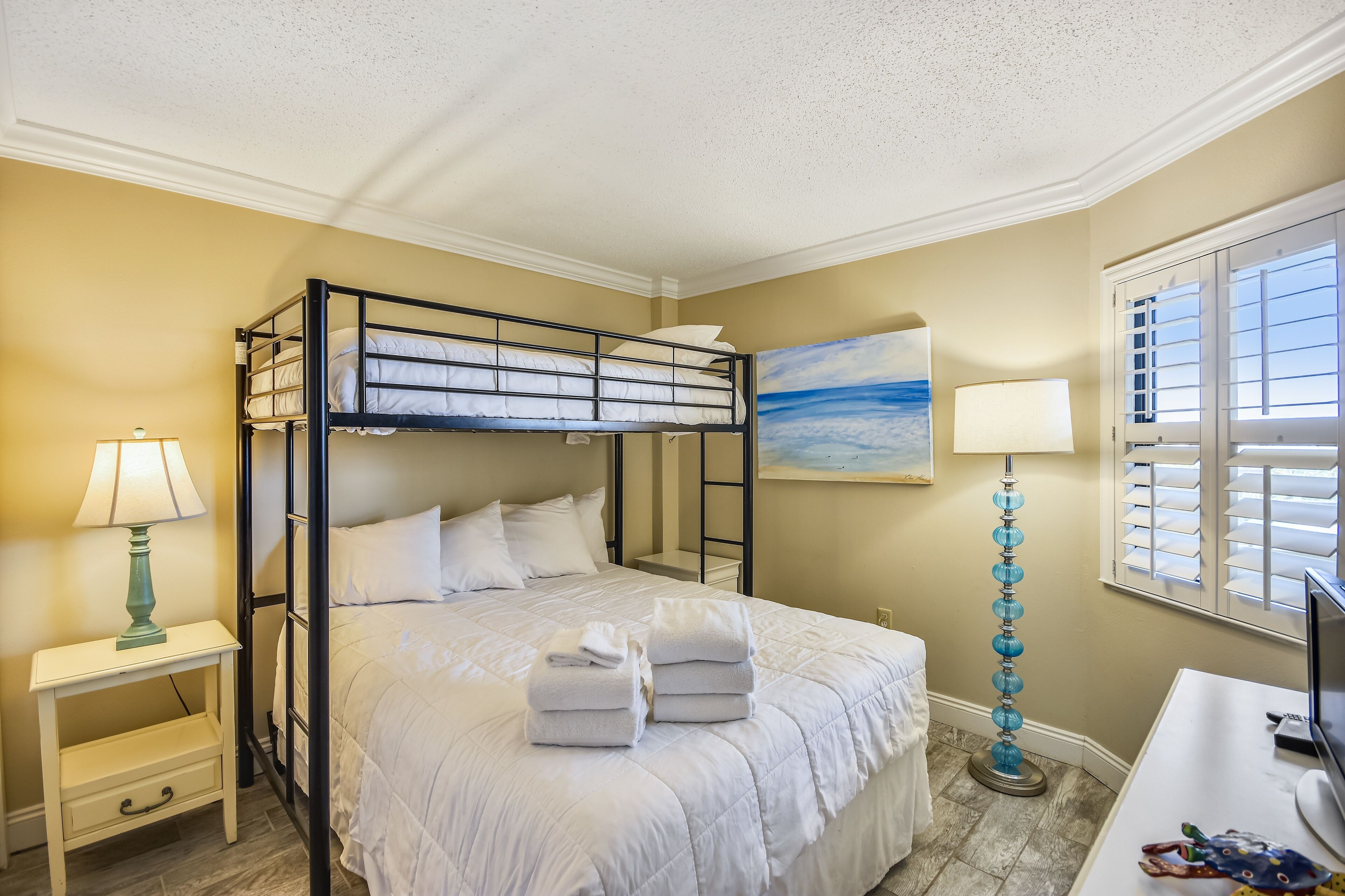 Une chambre avec un lit superposé, un bureau, une lampe et un tableau au mur.