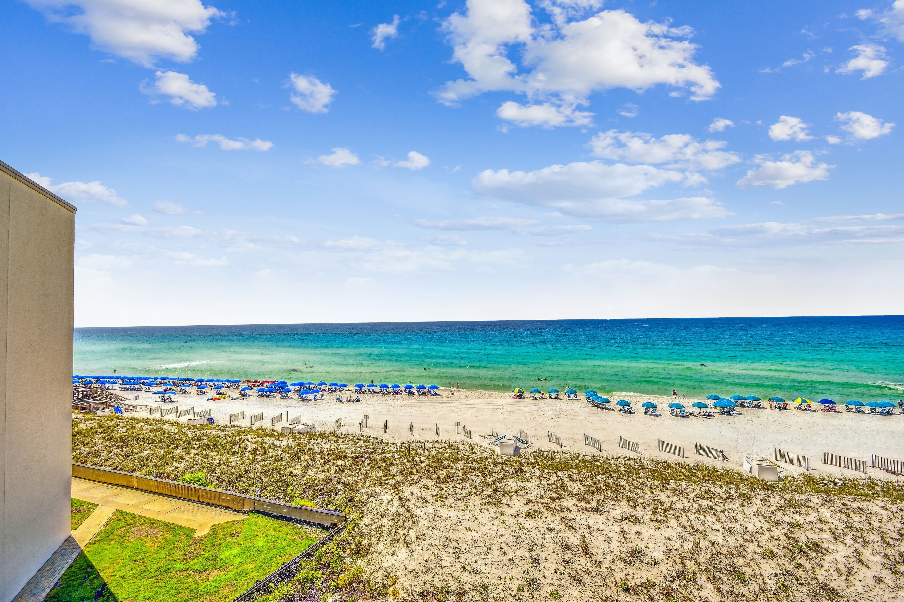 A beach view with a clear sky, a sandy beach, and umbrellas.