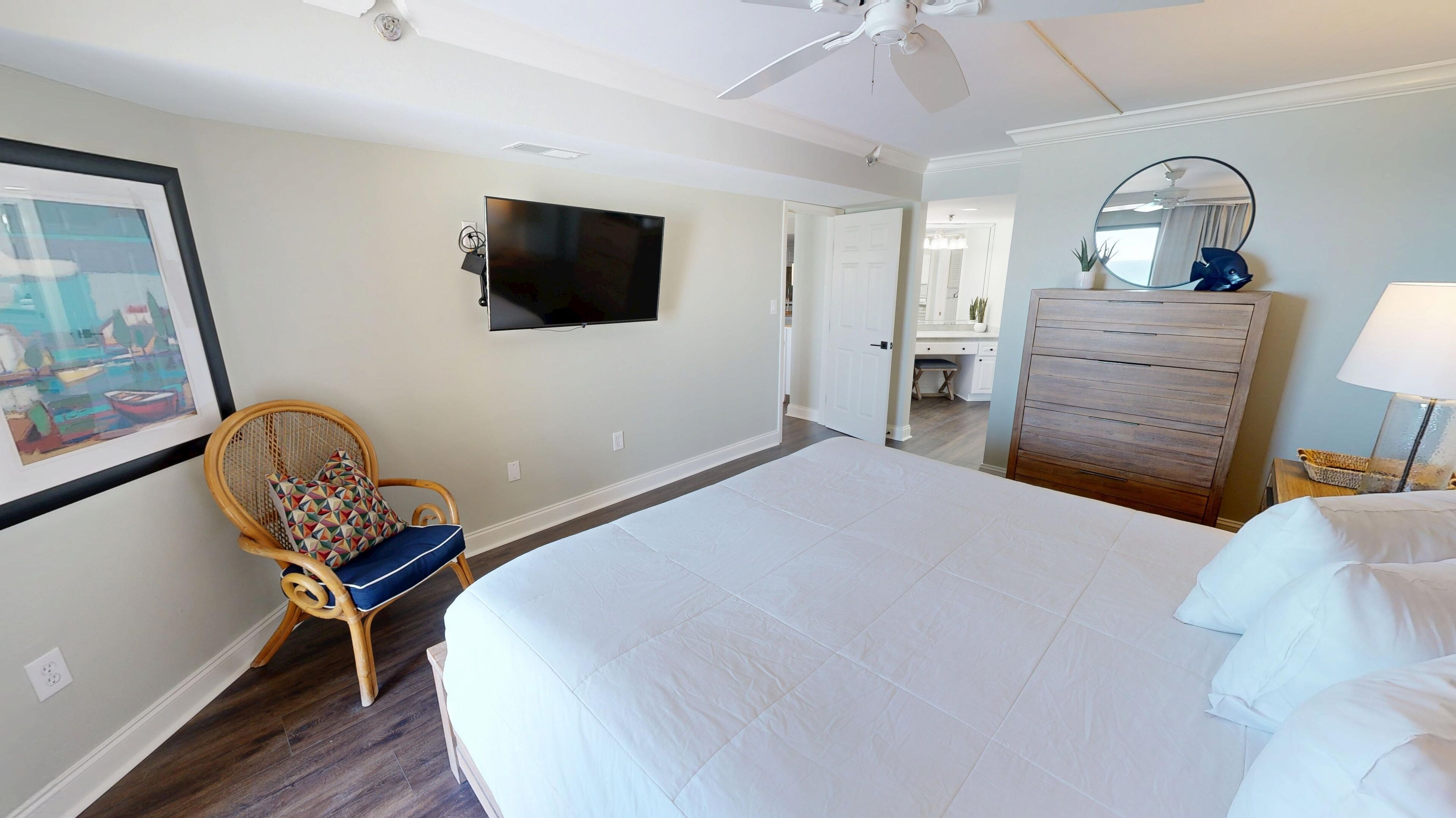A bedroom with a large bed, a television on the wall, a chair, a dresser, and a mirror.