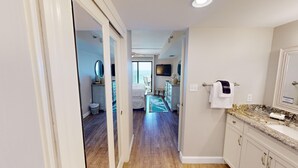 A hotel room with a balcony, a TV, a bathroom with a marble countertop, and a hallway leading to another room.
