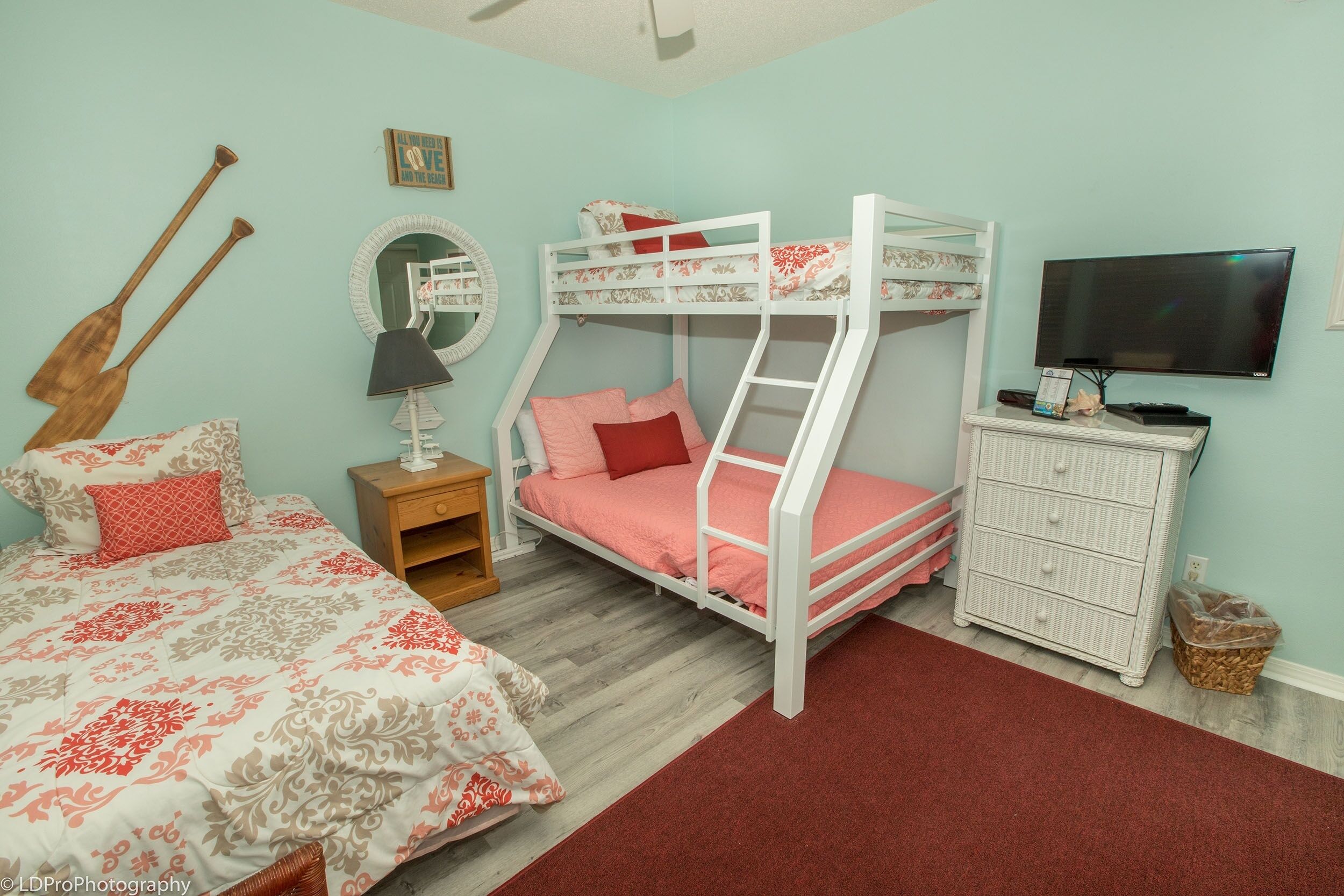A bedroom with bunk beds, a television, a dresser, a mirror, and a wooden paddleboard.