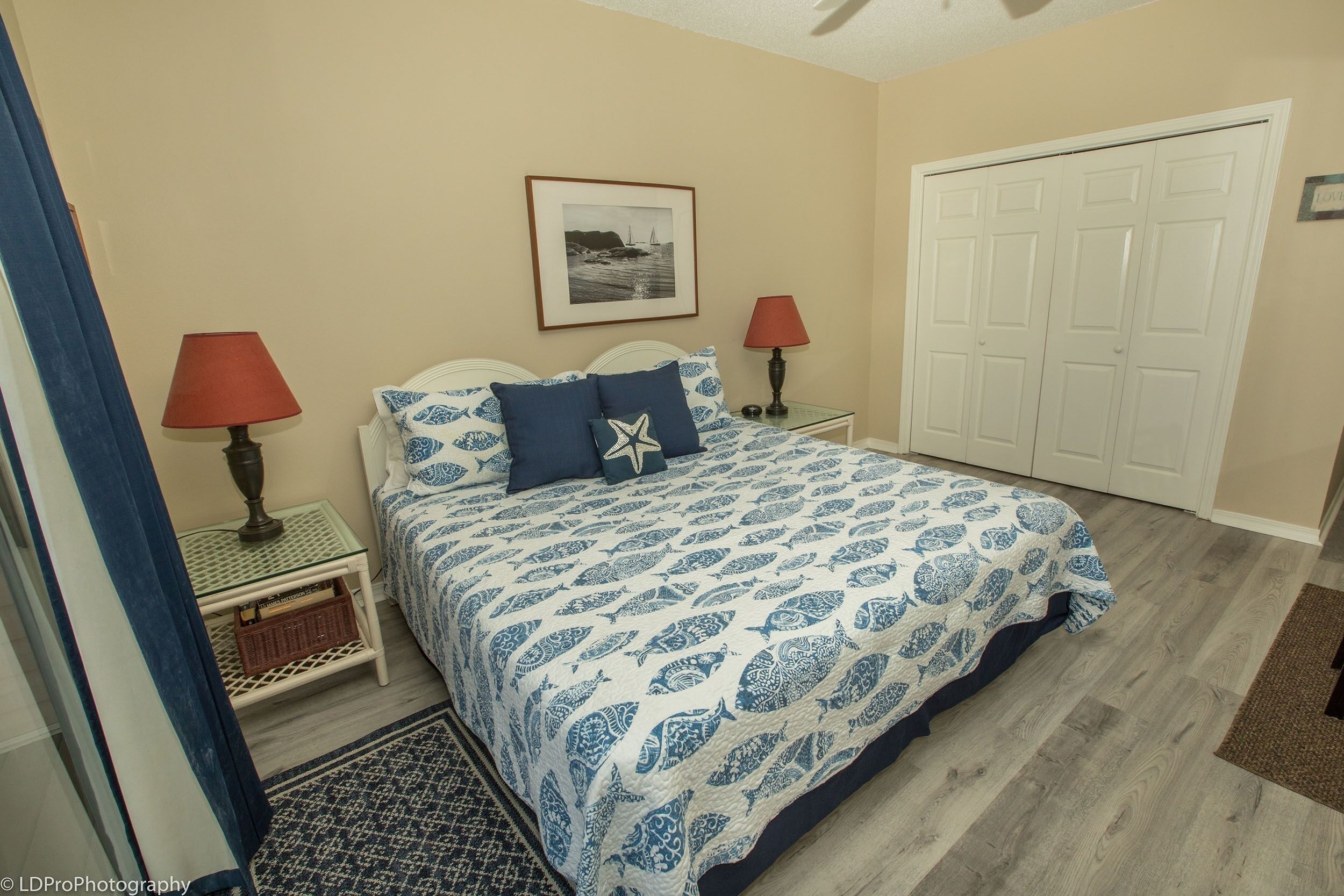 A bedroom with a bed, two bedside tables with lamps, a framed picture on the wall, and a closet.