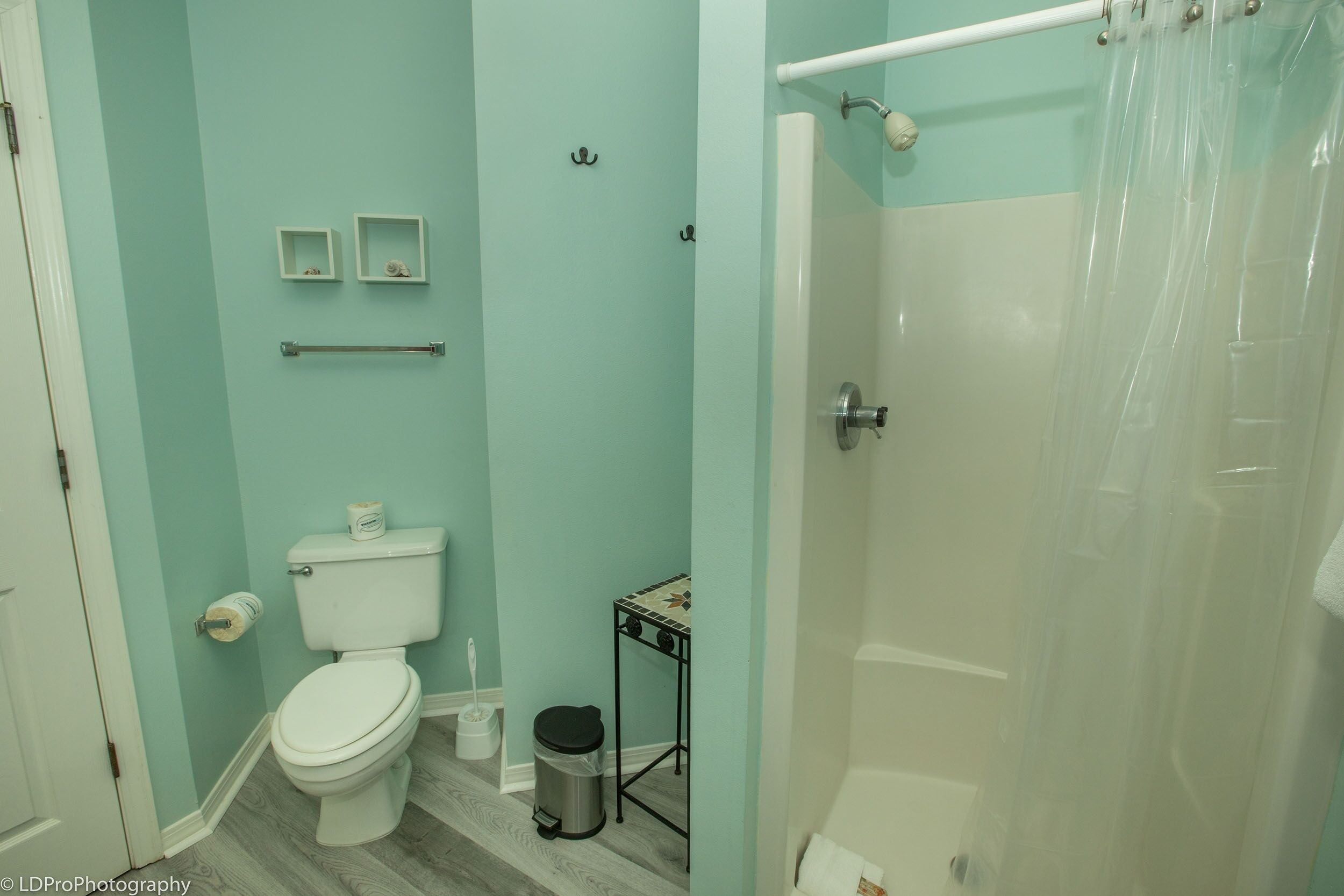 Une salle de bain comprenant des toilettes, une poubelle, une petite étagère avec des articles de toilette et un espace douche séparé par un rideau.
