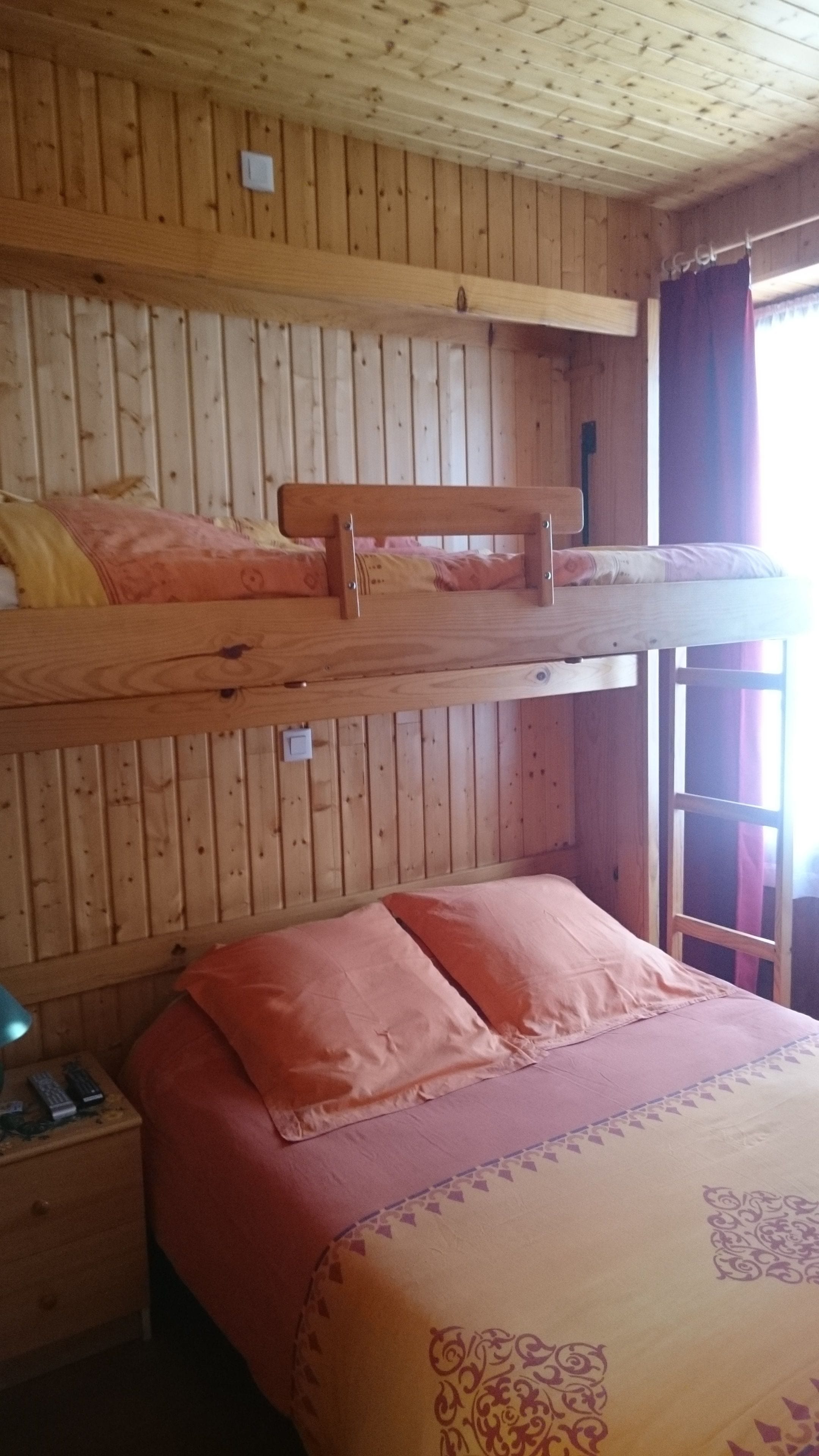 A bunk bed room with wooden walls and a window with curtains.