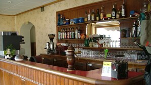 A bar area with a wooden counter, shelves with bottles, glasses, and a sign indicating a tariff bar. - Résidence Le Bellevue (Fourneaux)