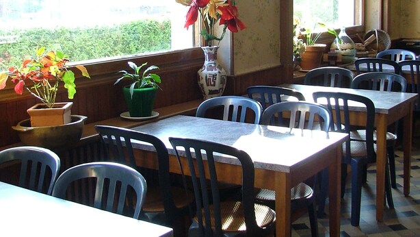 A restaurant with multiple tables and chairs, large windows with views of greenery, and potted plants on the windowsill. - Résidence Le Bellevue (Fourneaux)