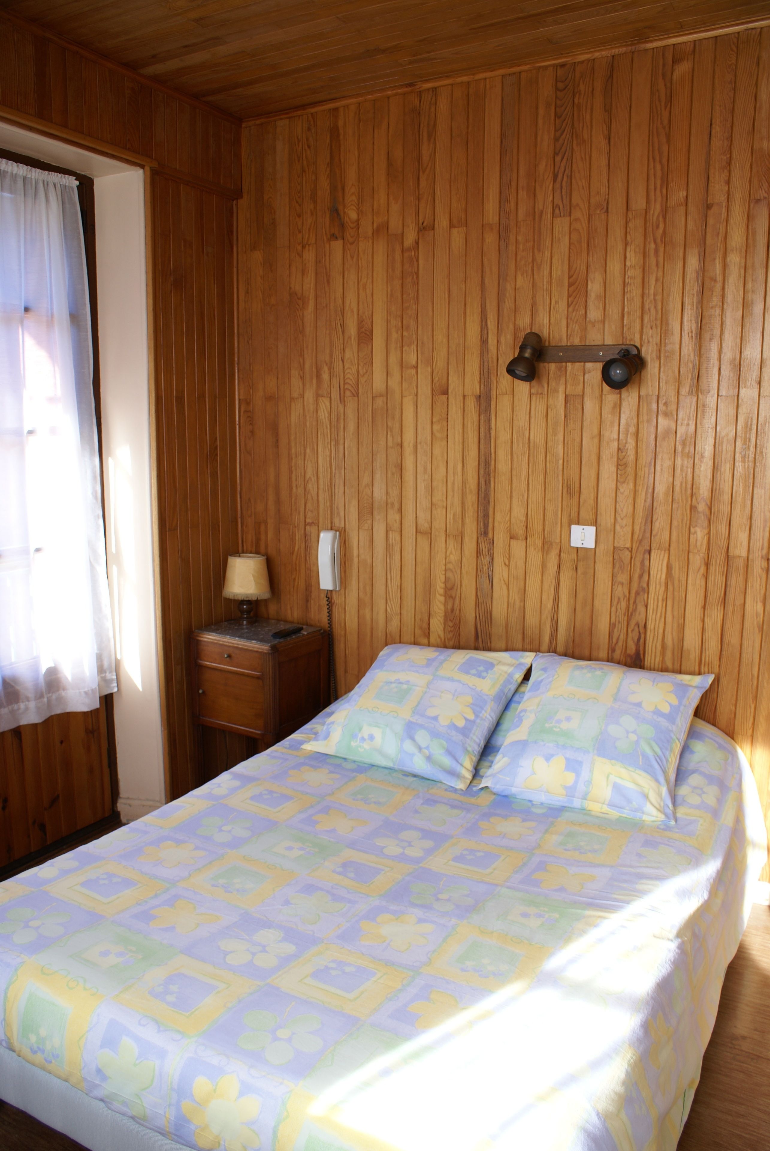 A wooden-paneled room with a bed, a nightstand, a lamp, and a telephone.