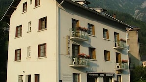 A two-story hotel with balconies, a sign indicating it is a hotel, and a mountainous backdrop. - Résidence Le Bellevue (Fourneaux)
