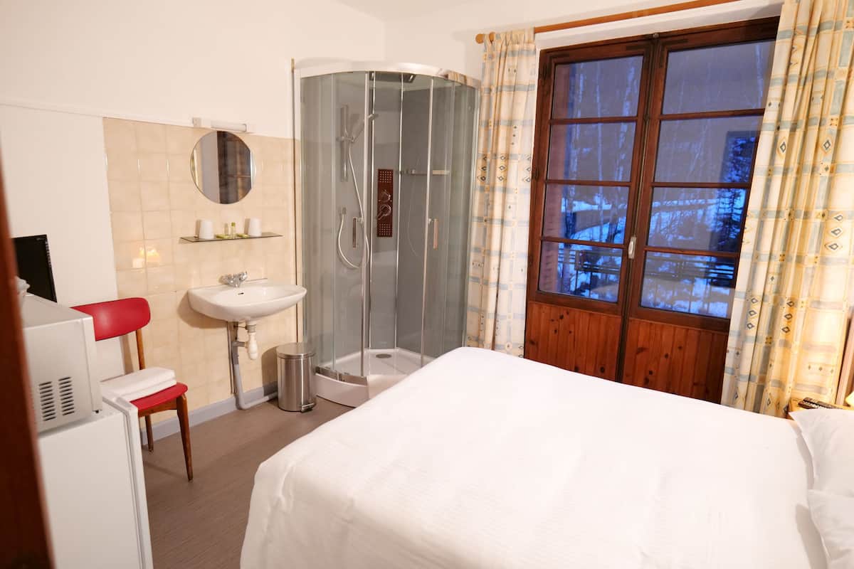 Een hotelkamer met een bed, een douche, een wastafel, een spiegel en een raam met gordijnen.