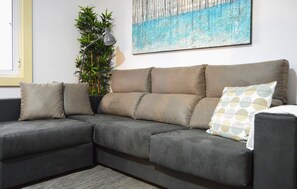 Un sofá modular con una combinación de colores gris y beige, una planta en maceta y un cuadro en la pared.