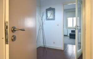 Una puerta con cerradura y manija, que da a un cuarto con pared blanca, un cuadro enmarcado y un espacio habitable visible con un sofá y un radiador.