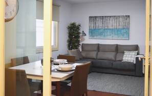 Una sala de estar con un sofá gris, una mesa de comedor con sillas, un reloj y un cuadro en la pared.