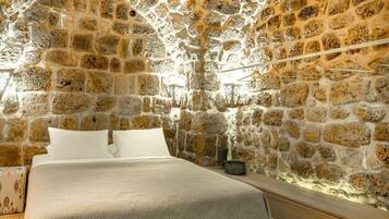 A stone-walled room with a bed, a small table, and a hanging light fixture.