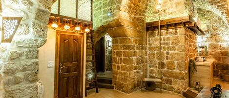 A stone-walled room with a wooden door, a staircase, and a table with a sewing machine.