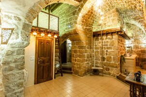 Una habitación con paredes de piedra, una puerta de madera, una escalera y una mesa con una máquina de coser.