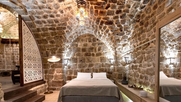 A stone-walled bedroom with a bed, a large mirror, and a decorative partition. - Zidan Sarai Suite (Acre)