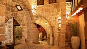 A stone-walled interior with a wooden table, a patterned rug, and a large vase. - Zidan Sarai Suite (Acre)