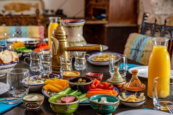 Una mesa dispuesta con diversos platos, incluyendo pan, verduras y una jarra de jugo de naranja, sugiriendo una preparación para comer.
