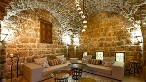 A stone-walled room with a sofa, two round tables, and a patterned rug. - Zidan Sarai Suite (Acre)