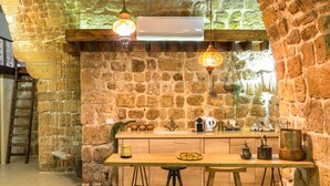 A rustic kitchen with stone walls, wooden bar stools, and hanging pendant lights. - Zidan Sarai Suite (Acre)