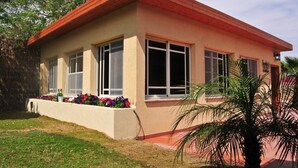 A single-story building with a red roof and beige walls, featuring large windows and a small garden area with colorful flowers. - Idan Lodge In The Arava (HaArava HaTikhona)