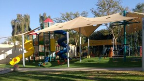 A playground with slides and climbing structures, surrounded by grass and trees. - Idan Lodge In The Arava (HaArava HaTikhona)