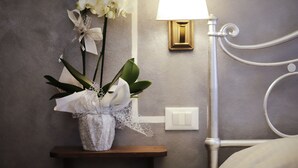 Ein Nachttisch mit einer weißen Orchideen-Vase, eine Wandlampe und ein Bett mit weißem Kopfteil.